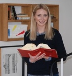 Eine junge Rechtspflegerin hält ein Gesetzbuch in der Hand und lächelt in die Kamera