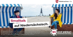 Smalltalk auf Niedersächsisch: Ein älterer Mann und eine junge Frau sitzen in einem Strandkorb und unterhalten sich (Verlinkung zu https://impfen-schuetzen-testen.de/)