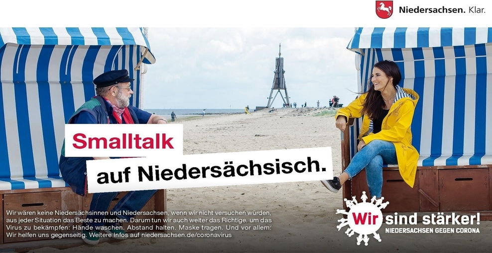 Smalltalk auf Niedersächsisch: Ein älterer Mann und eine junge Frau sitzen in einem Strandkorb und unterhalten sich (Verlinkung zu https://impfen-schuetzen-testen.de/)